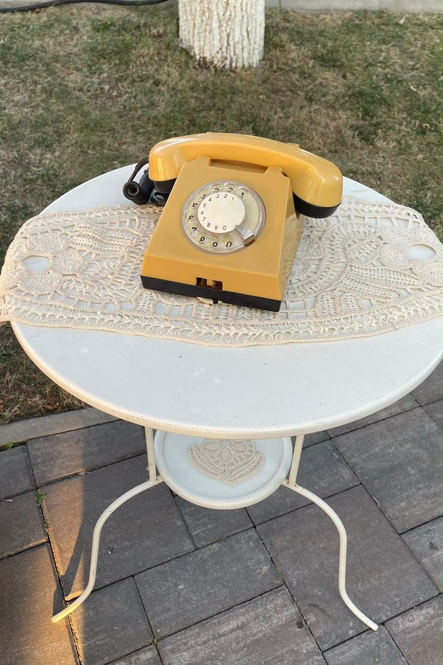 Telefon cu disc, crem, așezat pe un șervet de dantelă, pe o măsuță albă de fier