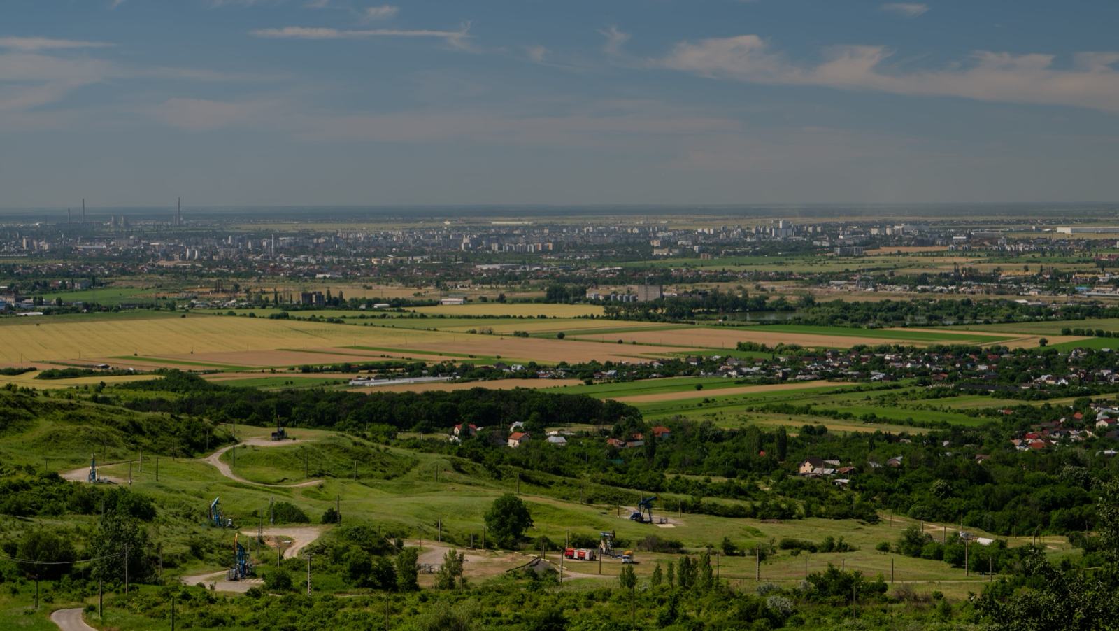Câmpia văzută de pe deal, cu ogoare, sate și dealuri în zare